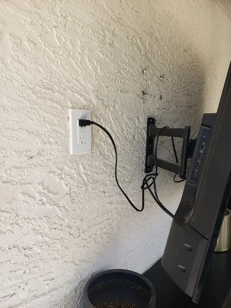 White outlet with black cable connected to TV mount on textured wall