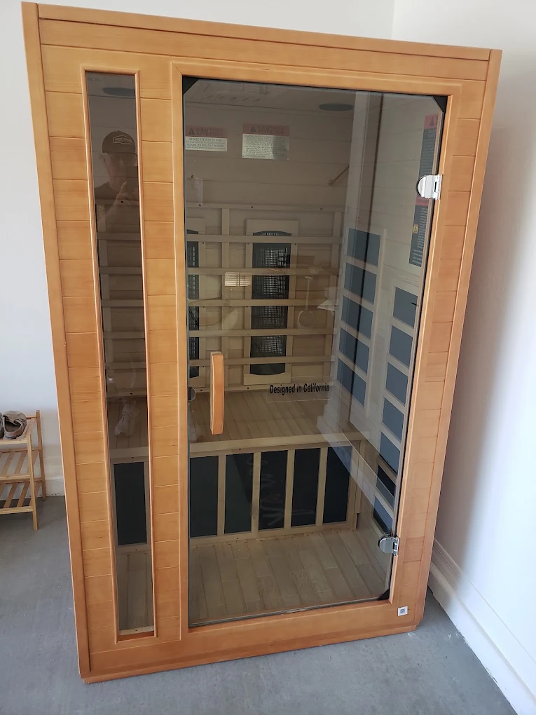 Infrared sauna cabinet with cedar wood frame and glass door, featuring interior benches and heating elements