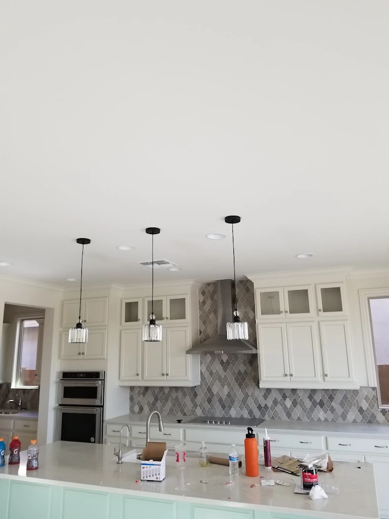 Modern kitchen with white cabinets, gray diamond backsplash, dark range hood, and three pendant lights over island