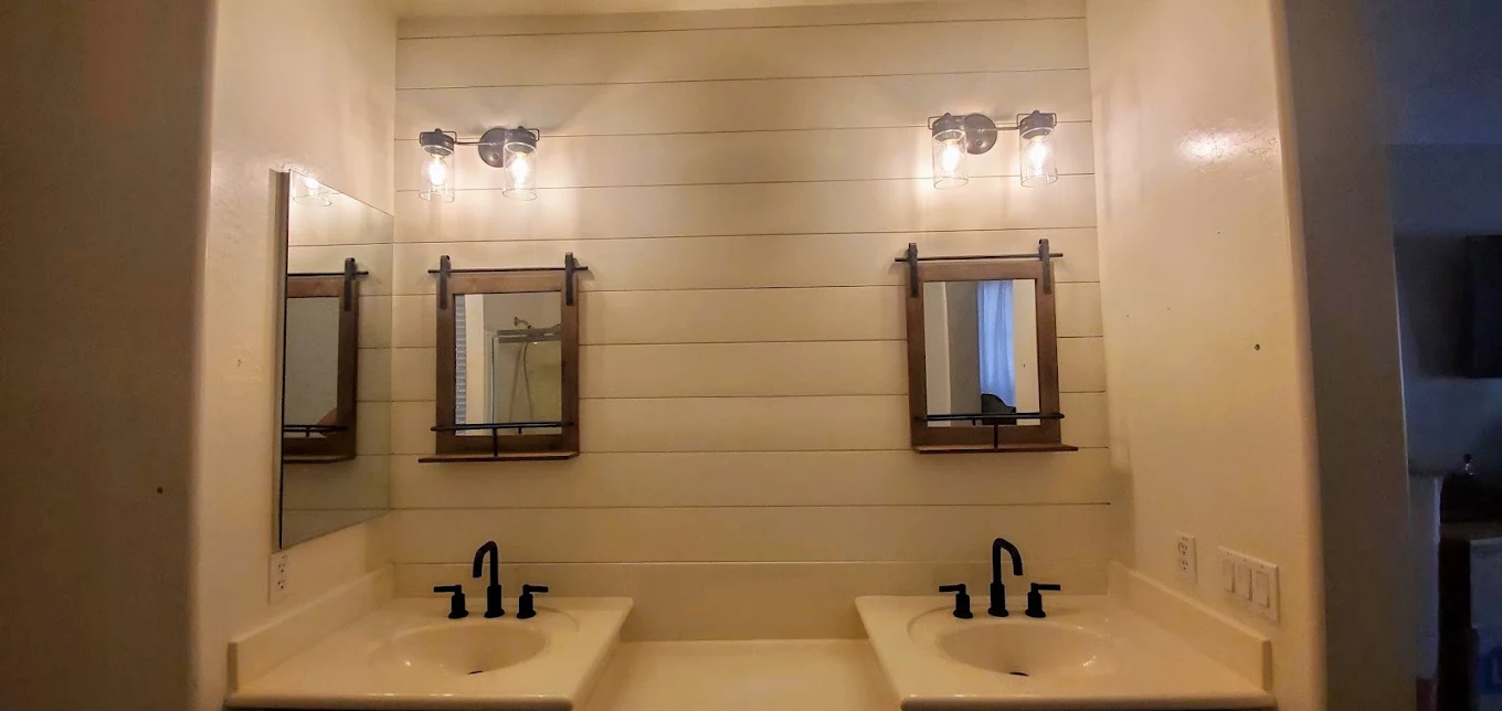Double vanity bathroom with cream countertops, black faucets, wooden-framed mirrors, and shiplap walls