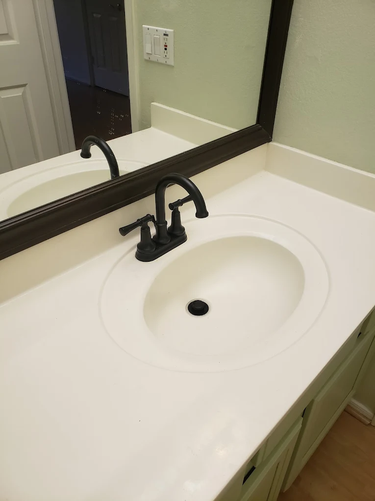 White bathroom sink with black faucet and mirror in light green tiled bathroom