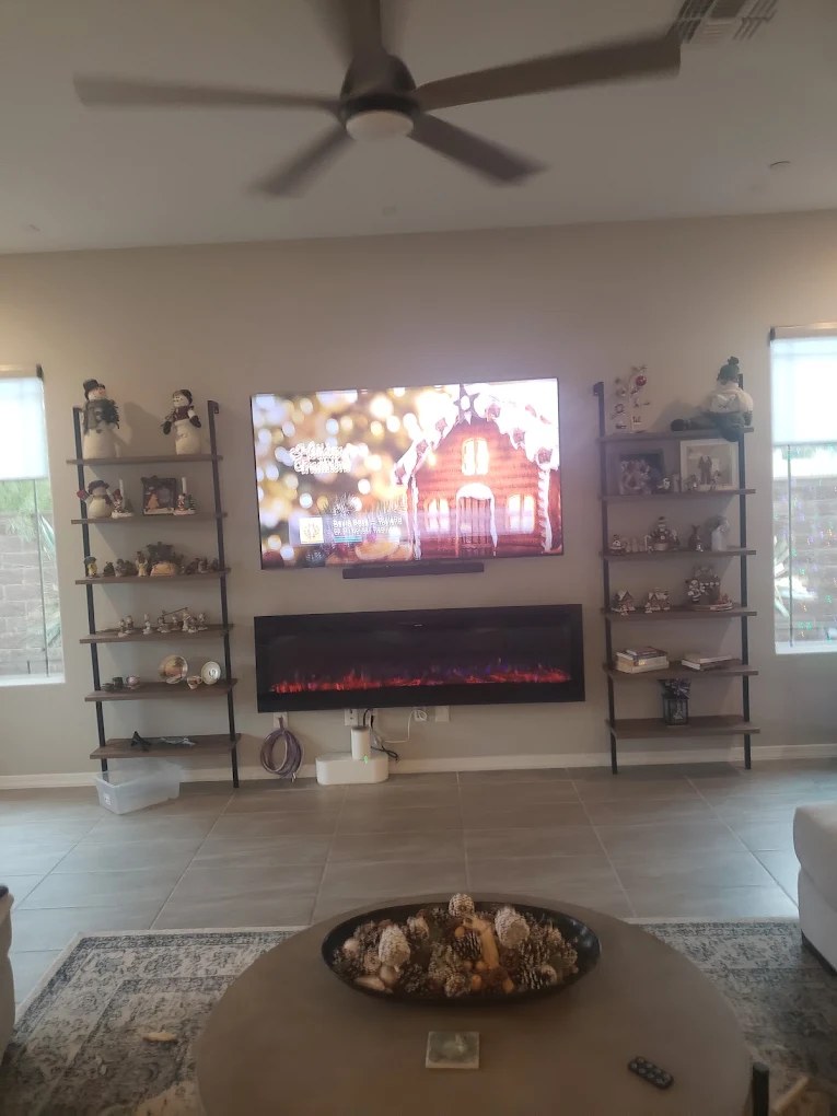 Modern living room with fireplace, TV, shelving units, and ceiling fan