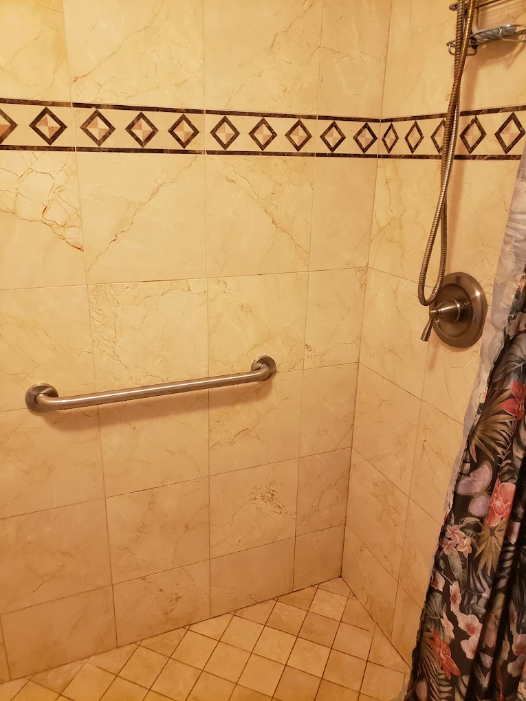Accessible shower with grab bar and decorative tile border in cream marble bathroom