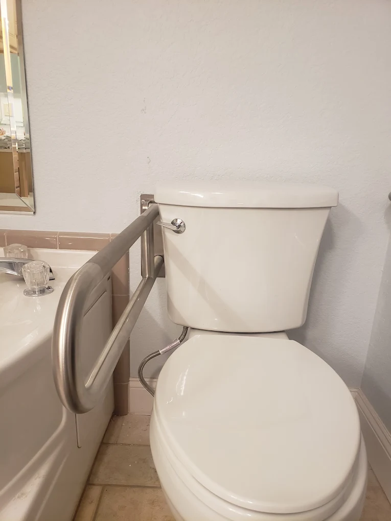 White ceramic toilet with closed lid in a bathroom with grab bar and sink