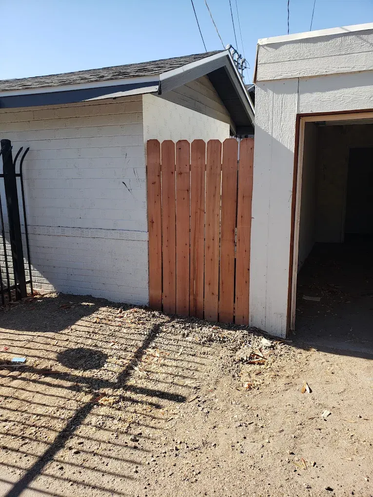 Residential driveway with white garage, weathered wooden gate, and side structure under clear sky