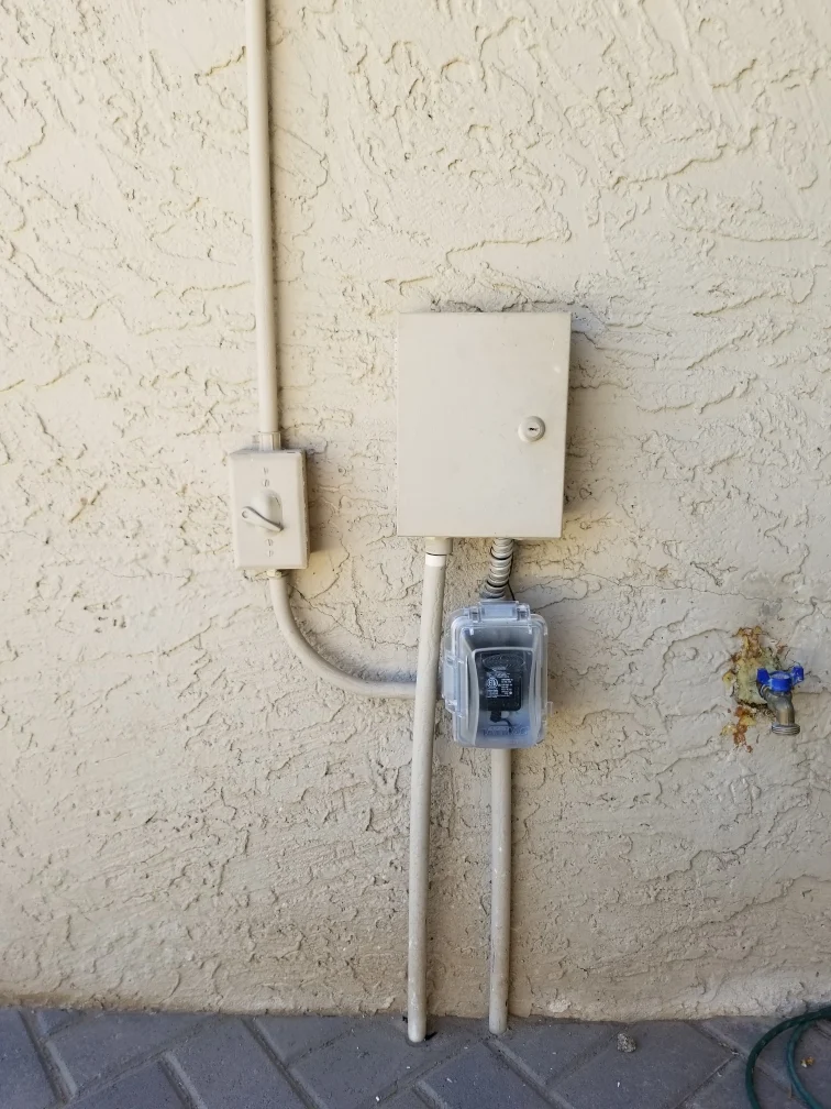 Outdoor electrical panel mounted on textured stucco wall with conduit and weatherproof outlet box