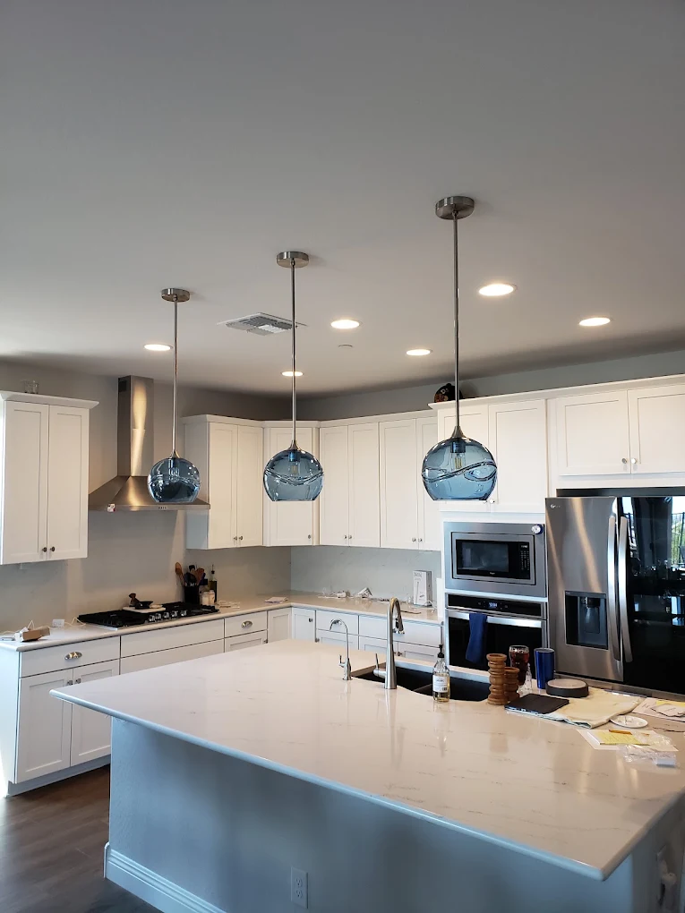Modern kitchen with white cabinetry, island, stainless steel appliances, and three blue glass pendant lights