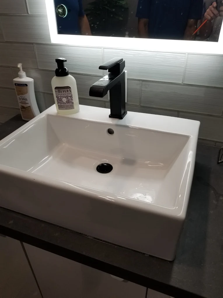 Modern white rectangular bathroom sink with black faucet and soap dispensers