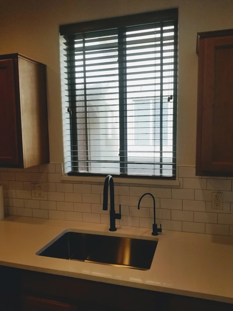 Modern kitchen sink with black faucet and window shutters above counter
