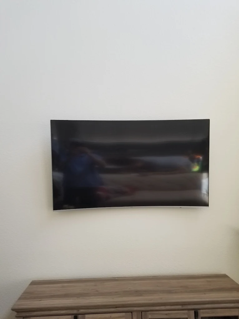 Curved flat-screen TV mounted on white wall above wooden media console