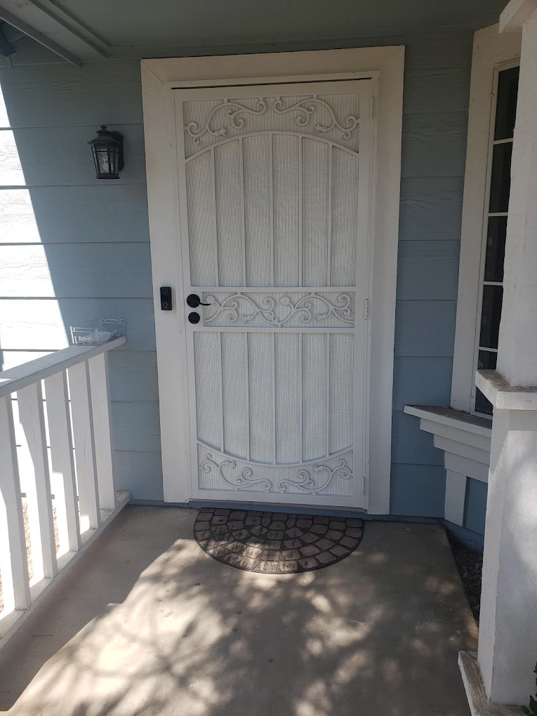 White ornamental screen door with scrollwork on blue siding porch
