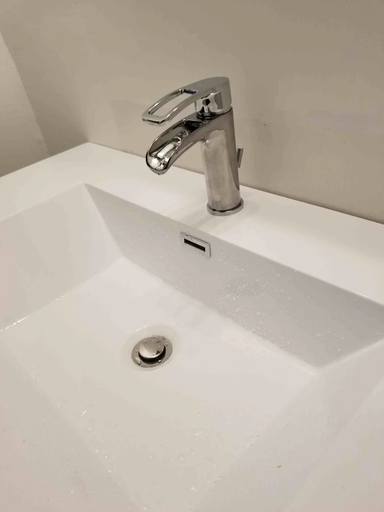 Modern chrome bathroom sink faucet over white rectangular basin with drain