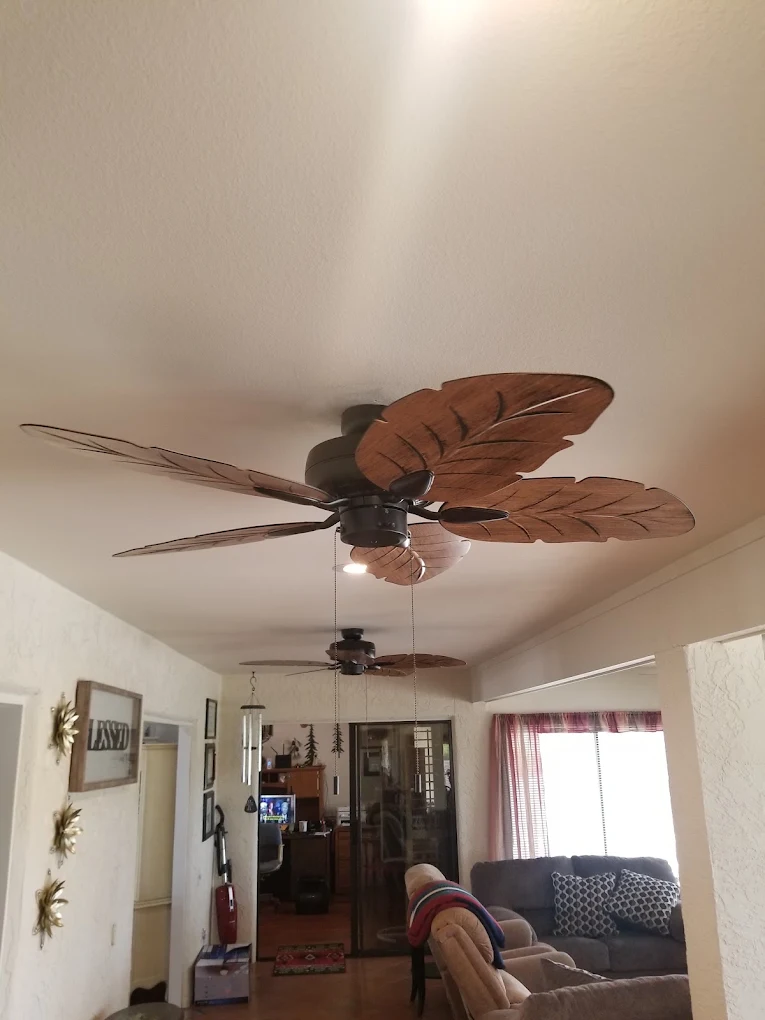 Tropical leaf-shaped ceiling fan with brown blades mounted on white ceiling in living room