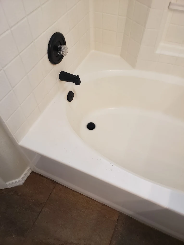 Bathtub with black shower fixtures and controls mounted on white tile wall