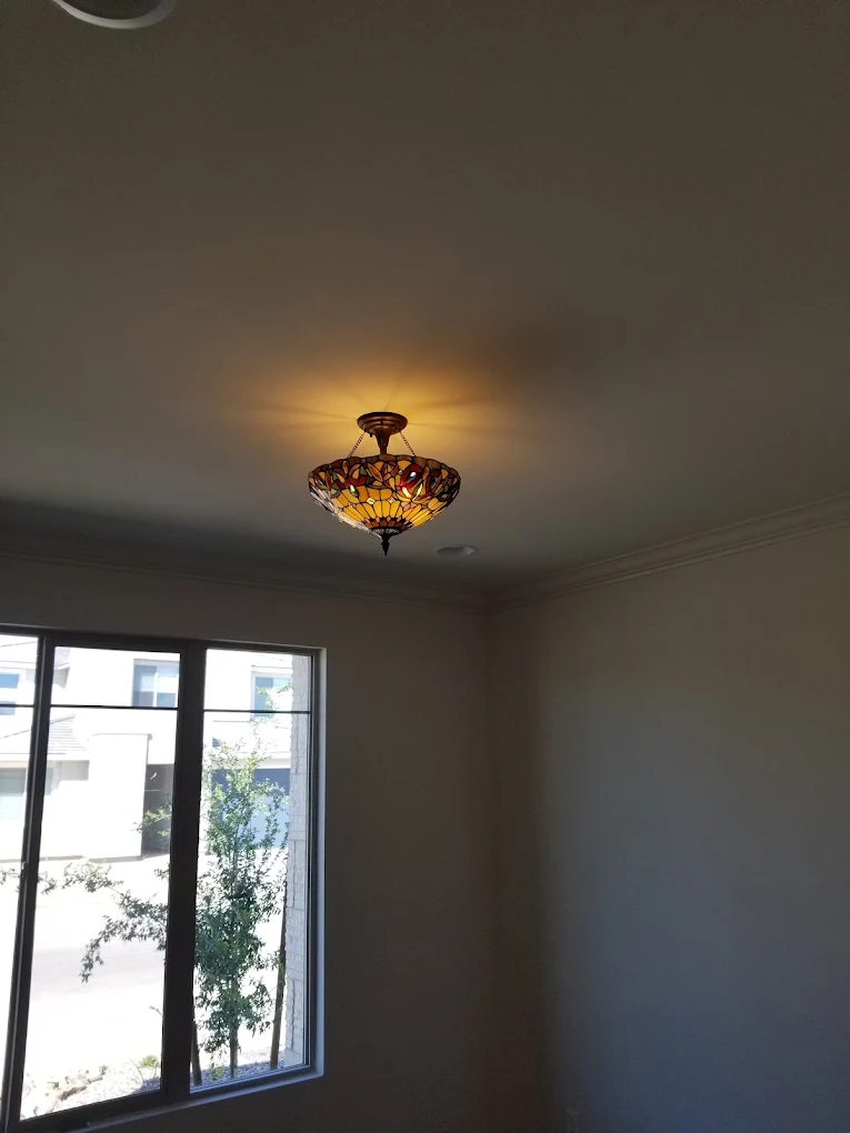 Tiffany-style stained glass ceiling fixture illuminating beige room with windows overlooking courtyard