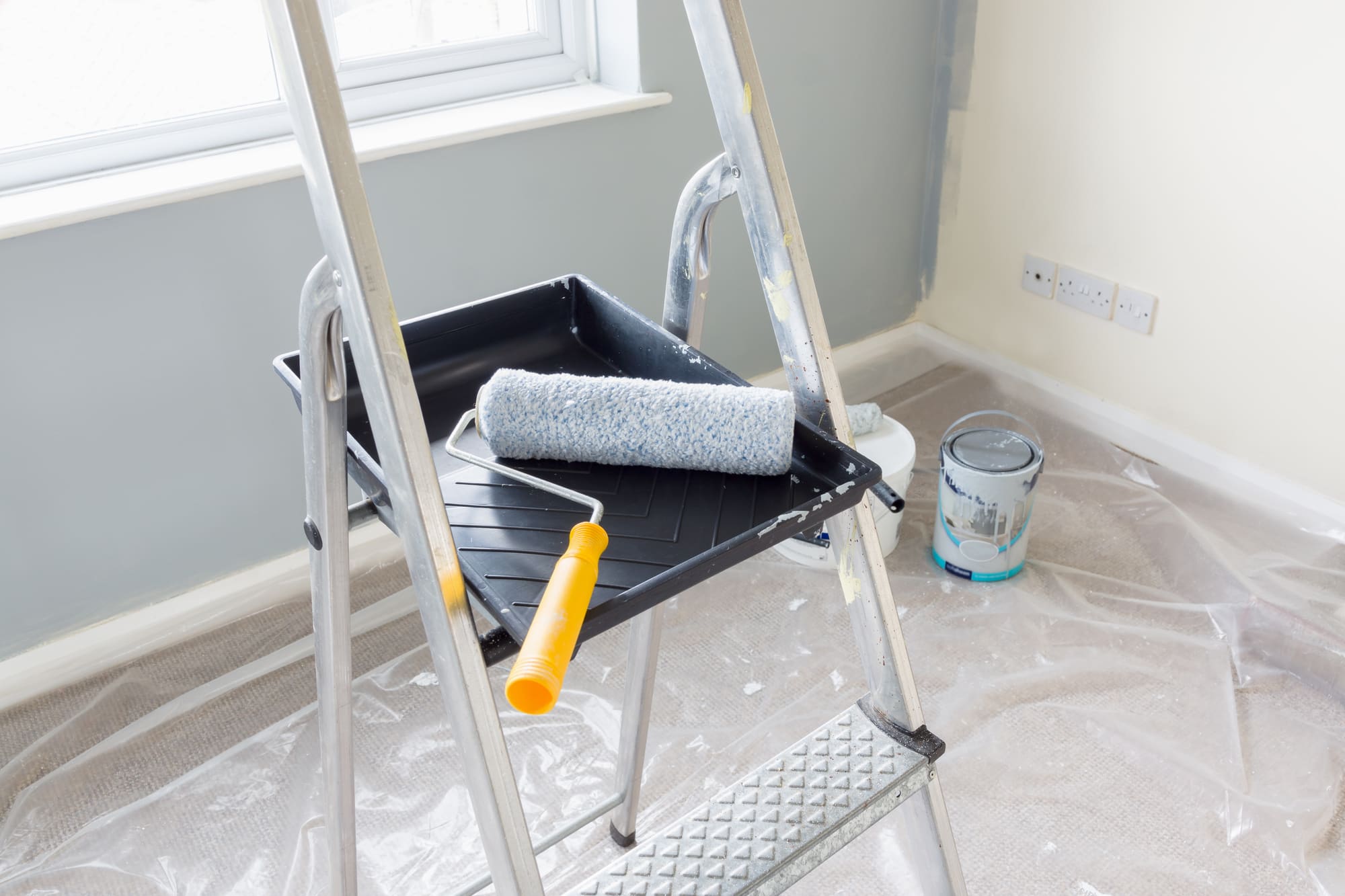 Painter's ladder with roller tray, paint roller, cloth, and paint can in room under renovation