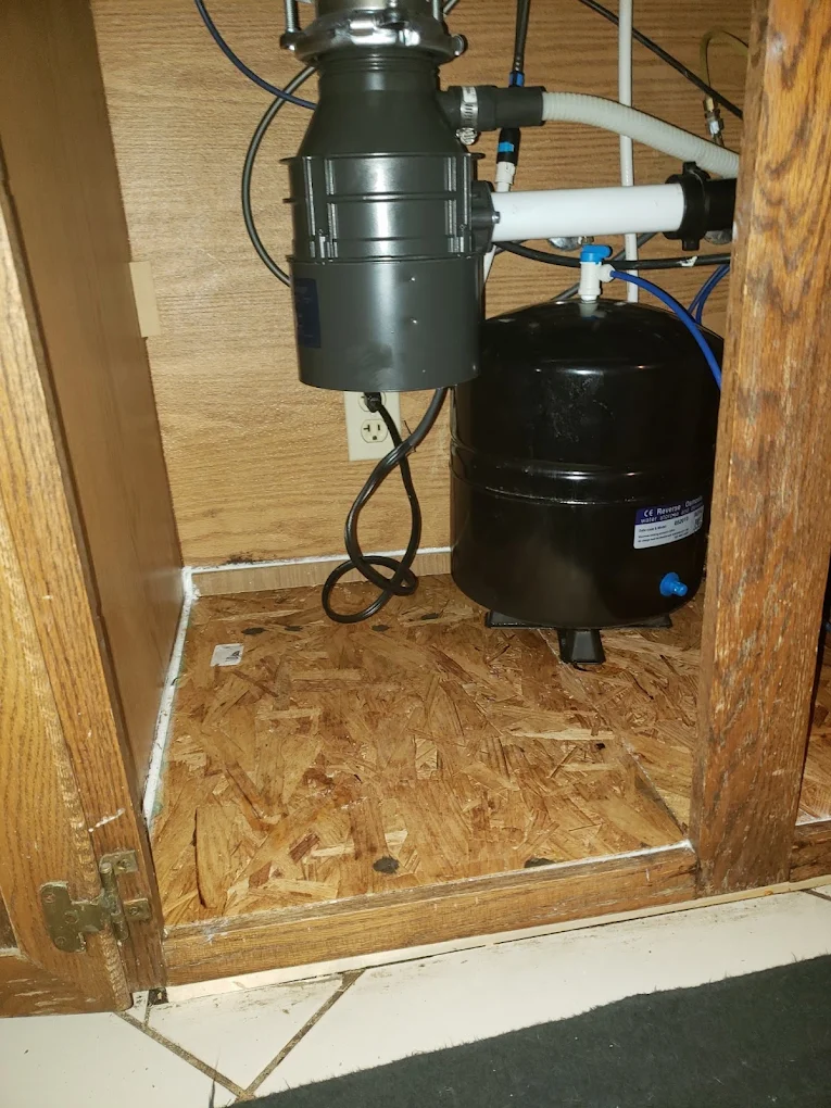 Under-sink garbage disposal and black storage tank installation with white piping
