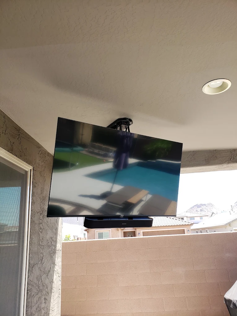 Flat-screen TV mounted on exterior concrete wall displaying pool scene
